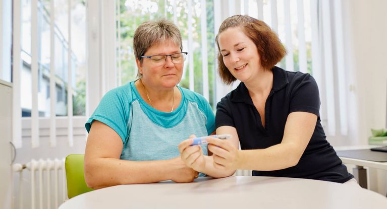Eine Diabetesberaterin und eine Patientin sitzen am Tisch und sprechen über eine Insulinspritze