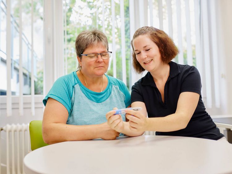 Eine Diabetesberaterin und eine Patientin sitzen am Tisch und sprechen über eine Insulinspritze