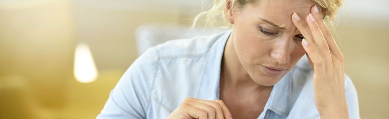 Eine erschöpfte Frau vor einem Laptop hält ihre Hand an der Stirn