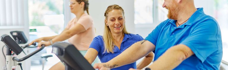Im Sportpark der Klinik zeigt eine Therapeutin einem Patienten, wie er den Ergometer am besten nutzt