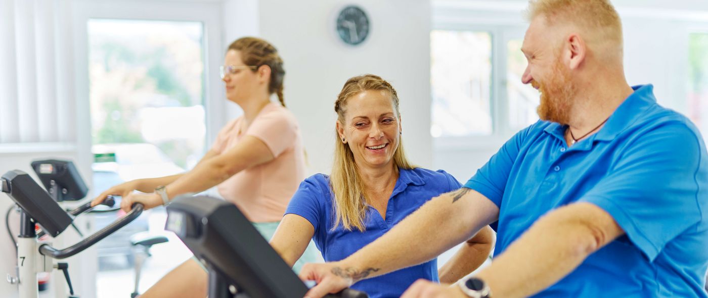 Im Sportpark der Klinik zeigt eine Therapeutin einem Patienten, wie er den Ergometer am besten nutzt
